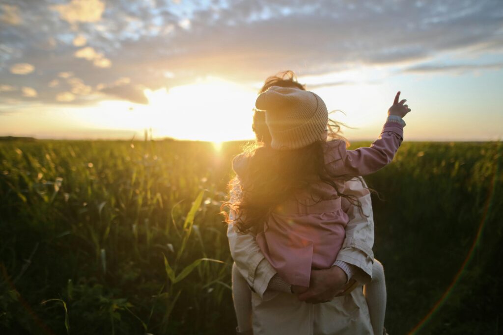 Mother holding young child in field looking at a sunset
