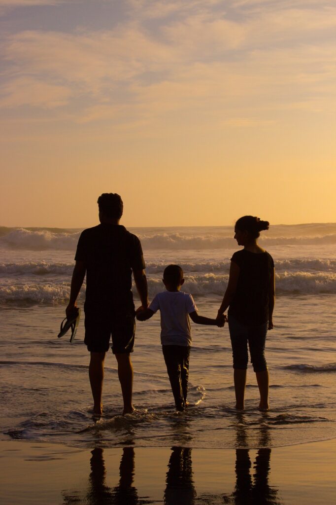 Family silhouettes enjoying a sunset at the beach and holding hands.