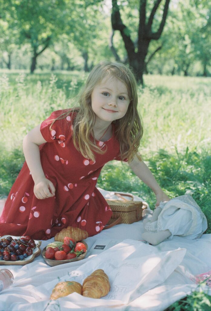 Picnic with kids Photo by Xander Miadelko A young girl enjoying a picnic outdoors with fruits and pastries in a lush garden setting.