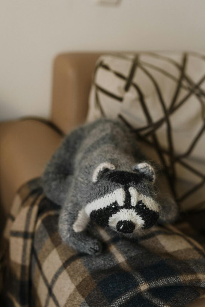 Gray raccoon stuffed toy with plaid blanket on sofa, perfect for cozy decor.
