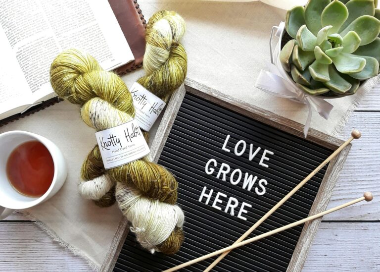 A cozy still life featuring yarn, tea, a succulent, and a book with a 'Love Grows Here' message representing low cost hobbies for parents