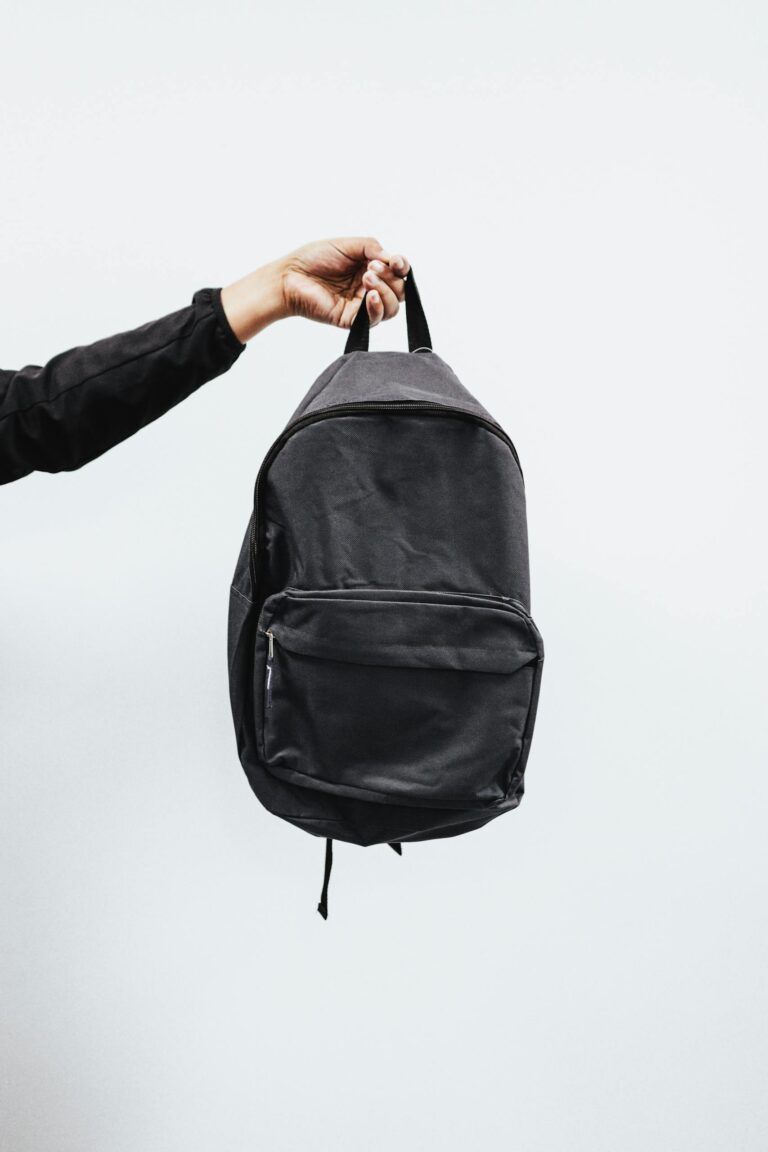 A simple black diaper bag backpack being held by a hand against a minimal white background, emphasizing style and practicality.