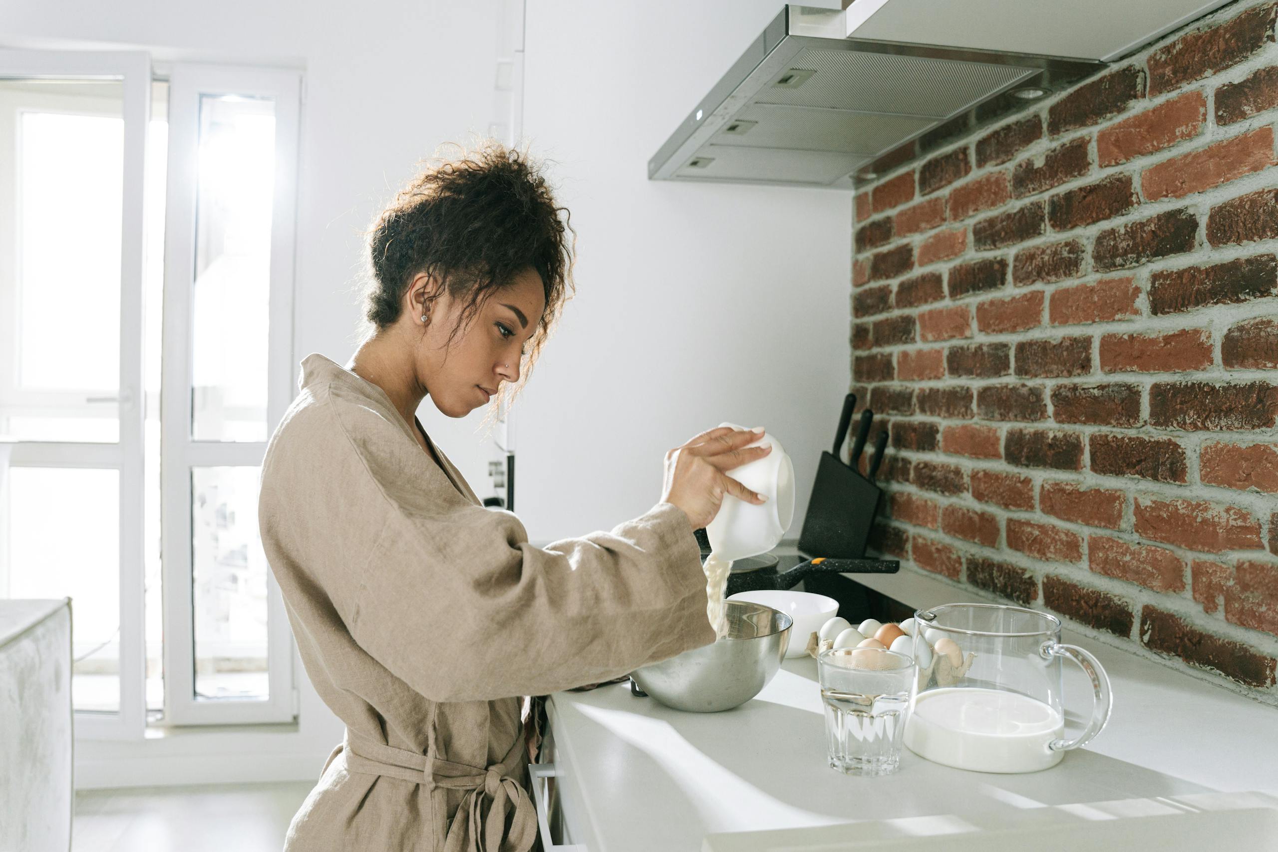 A woman mixing ingredients to make an easy baked breakfast in a sunny modern kitchen featuring a brick wall.