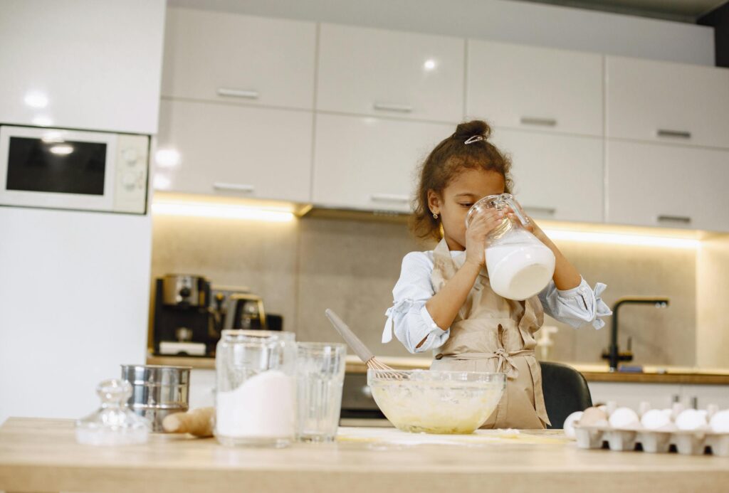 A young girl pours milk while helping mom make an easy baked breakfast in a contemporary kitchen environment.