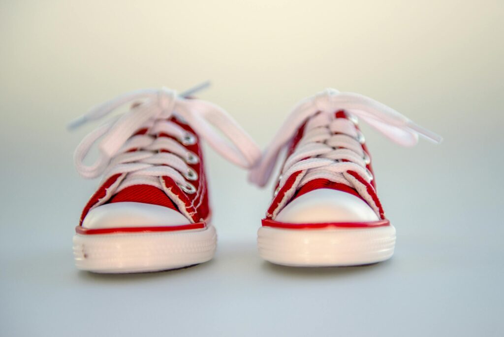 Close-up of bright red baby sneakers with white laces on a neutral background which are no longer kept in a diaper bag.