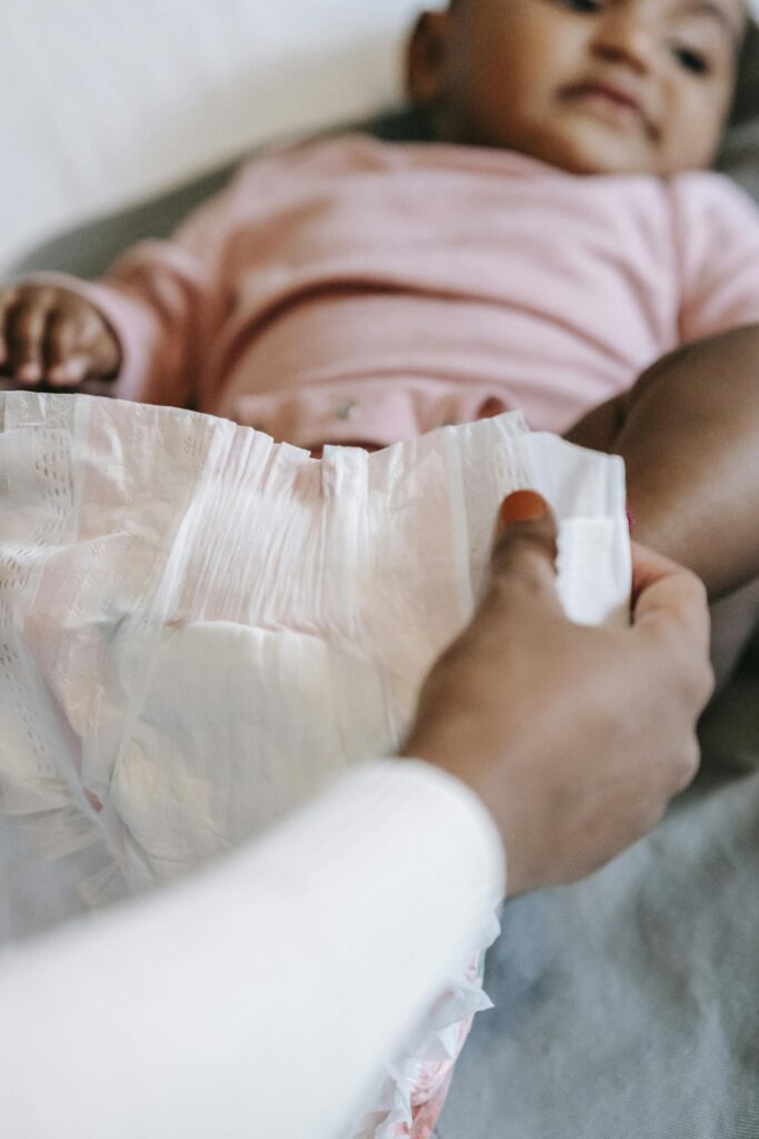 Crop anonymous ethnic mothers holding a diaper from the diaper bag while dressing calm baby lying on changing mat.